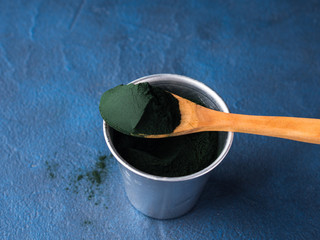 Spirulina super food powder in wooden spoon on blue background. Protein additive for smoothies