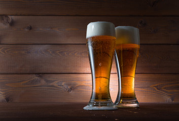 Two glasses of golden beer on wooden background