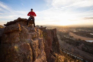 Adventurous man is rappeling down a cliff during a bright and vibrant sunny sunset. Taken in Smith...