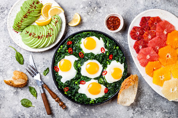 Green shakshuka with spinach, kale and peas. Healthy delicious breakfast with eggs, citrus salad, avocado. Top view, overhead, flat lay
