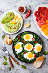 Green shakshuka with spinach, kale and peas. Healthy delicious breakfast with eggs, citrus salad, avocado. Top view, overhead, flat lay