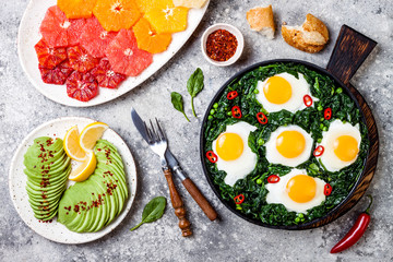Green shakshuka with spinach, kale and peas. Healthy delicious breakfast with eggs, citrus salad, avocado. Top view, overhead, flat lay