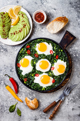 Green shakshuka with spinach, kale and peas. Healthy delicious breakfast with eggs, avocado. Top view, overhead, flat lay