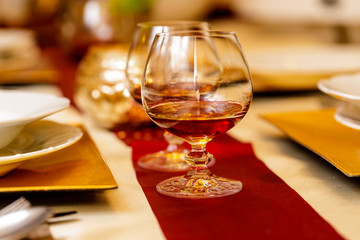 Brandy in two glasses on celebrate table, with plate. Christmas background