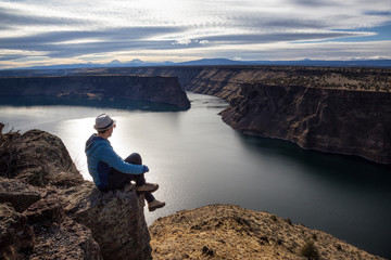 Fototapeta premium Man is sitting at the edge of a cliff and enjoying the beautiful landscape. Taken at The Cove Palisades State Park in Oregon, North America.