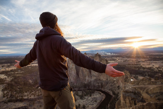 Adventurous man with open arms is enjoying the beautiful sunset from the top of the mountain. Taken in Smith Rock, Oregon, North America.