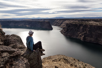 Man is sitting at the edge of a cliff and enjoying the beautiful landscape. Taken at The Cove Palisades State Park in Oregon, North America.