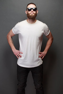 Hipster handsome male model with beard wearing white blank t-shirt with space for your logo or design over gray background
