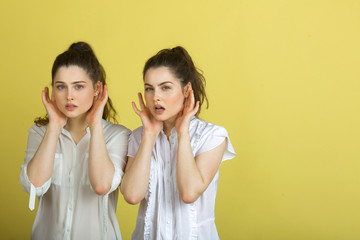 two beautiful young girl sisters twins in white blouses on a yellow background with expression on their faces