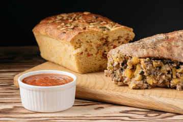 Pumpkin muffin and baked meat roll with filling along with a sauce on a wooden plate on a black background