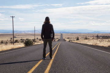 Obraz premium Man is standing in the middle of the long road during a vibrant sunny day. Taken in Oregon, North America.