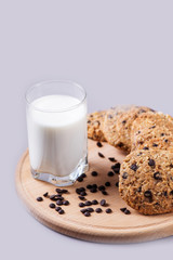 Homemade cookies on a round wooden plate with a glass of milk on a gray background