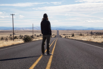 Obraz premium Man is standing in the middle of the long road during a vibrant sunny day. Taken in Oregon, North America.