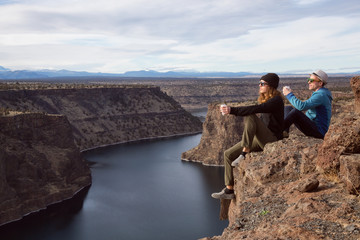 Friends sitting at the edge of a cliff and enjoying the beautiful landscape. Taken at The Cove Palisades State Park in Oregon, North America.