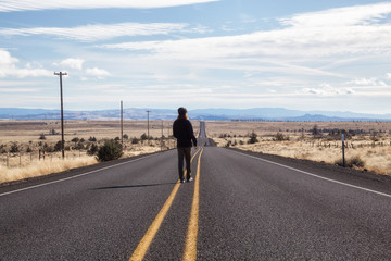 Obraz premium Man is standing in the middle of the long road during a vibrant sunny day. Taken in Oregon, North America.