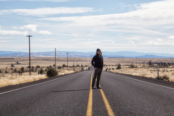 Obraz premium Man is standing in the middle of the long road during a vibrant sunny day. Taken in Oregon, North America.