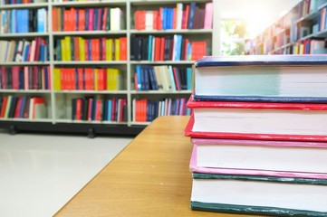 The old books on the wooden table in the library. Selective focus with blurred bookshelves and green leaves from the window background. Education concept. Selective focus.