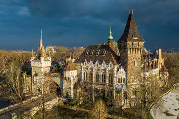 Fototapeta premium Budapest, Hungary - Aerial view of beautiful Vajdahunyad Castle in City Park at sunset with dark clouds behind at winter time