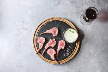 Grilled sliced rack of lamb with yogurt mint sauce served with glass of red wine, pink salt on round wooden slate board over grey texture background. Top view, space © Natasha Breen