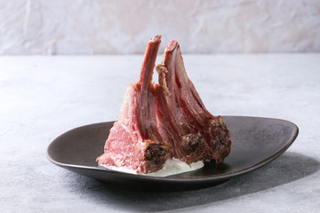 Grilled sliced rack of lamb with yogurt mint sauce served on ceramic plate over grey texture table....
