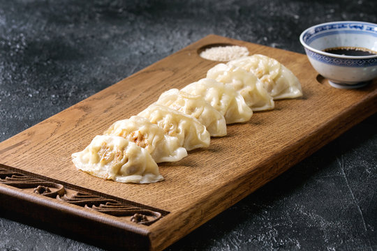 Asian dumplings Gyozas potstickers served with bowl of soy sesame sauce on asian style wooden board over black texture background. Close up.