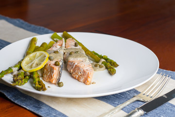 dish of cooked salmon with asparagus, lemon, capers and sauce on the plate