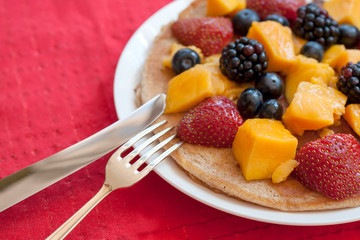 Pancake with fruit and berries in the plate on the red cloth