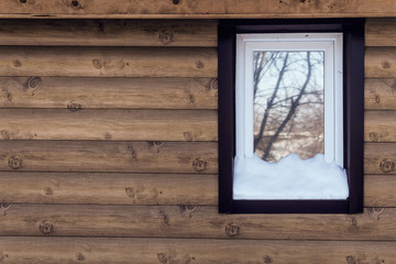 Plastic tinted window covered by snow on wooden wall background.