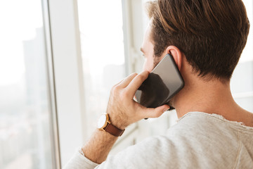 Closeup photo from back of man with short dark hair looking through window, while having mobile...