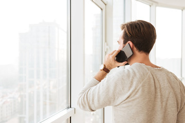 Photo from back of caucasian man with short brown hair looking through window, while speaking on...