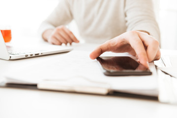 Cropped picture of man in white shirt taking off cell phone from table, while working at home or office