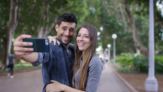 Young happy couple pose as they take a photo on their phone camera, in slow motion 