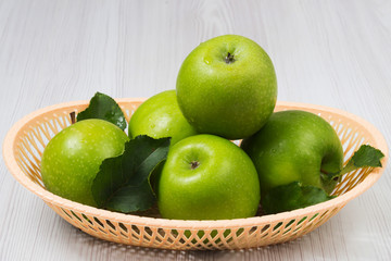 Green apples with leaves in a basket on white wooden table