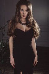 An attractive, slender, sexy brown-haired woman in a long black evening dress in the studio. Studio photo. Fashion photo.