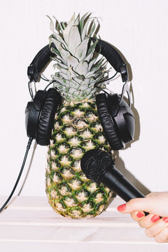 pineapple in earphones hand with microphone stretches to pineapple in earphones