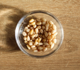 Glass bowl with pine nuts on wooden background