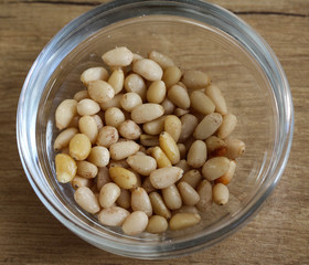 Glass bowl with pine nuts on wooden background