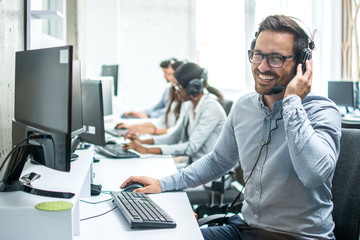 Smiling handsome customer support operator with headset working in call center.