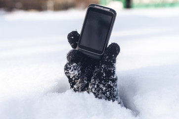 Mobile phone with blank screen copy space in the hand stretching out from under the snow. Contact...