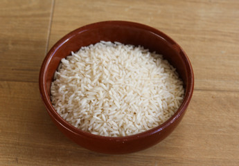 Fototapeta na wymiar Stone bowl with uncooked white rice on wooden background