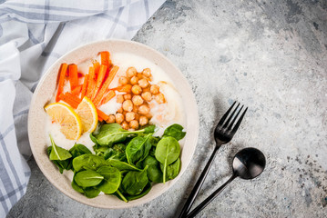 Modern vegan food, savory yogurt bowl with beans, chickpeas, spinach, spicy carrots, lemon, Gray stone background, copy space top view