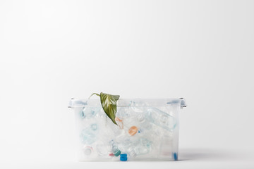 close up view of container with plastic bottles and green leaf isolated on grey, recycling concept