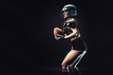 Fototapeta na wymiar Sportive serious woman in helmet of rugby player holding ball in stuio on dark background.