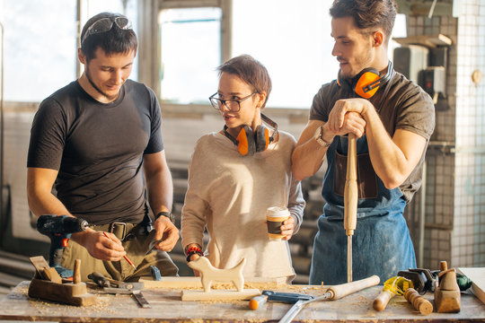male carpenter showing something to coworker at his notebook papers in workshop