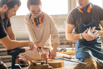 male carpenter showing something to coworker at his notebook papers in workshop