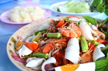 Spicy seafood and salted egg salad with sticky rice and some vegetable on blue table background.Delicious Thai menu with nutritional value of ingredient.Concept is healthy Thai food,for restaurant.