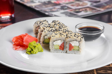 Serving of sushi on a white plate with wasabi, marinated ginger, soy sauce for filing in a cafe, restaurant. Serving dishes, delicious lunch, dinner, snacks