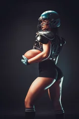  Sportive serious woman in helmet of rugby player holding ball in stuio on dark background. © zamuruev