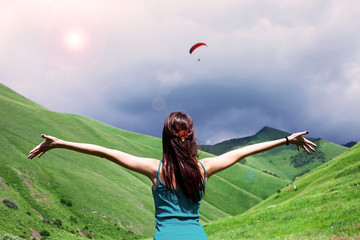 Girl is looking at the paraglider in the mountains
