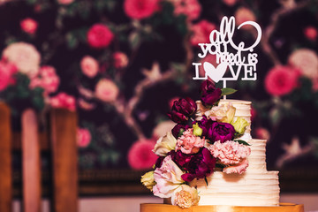 Three-tiered wedding cake decorated with beautiful flowers and wooden inscription